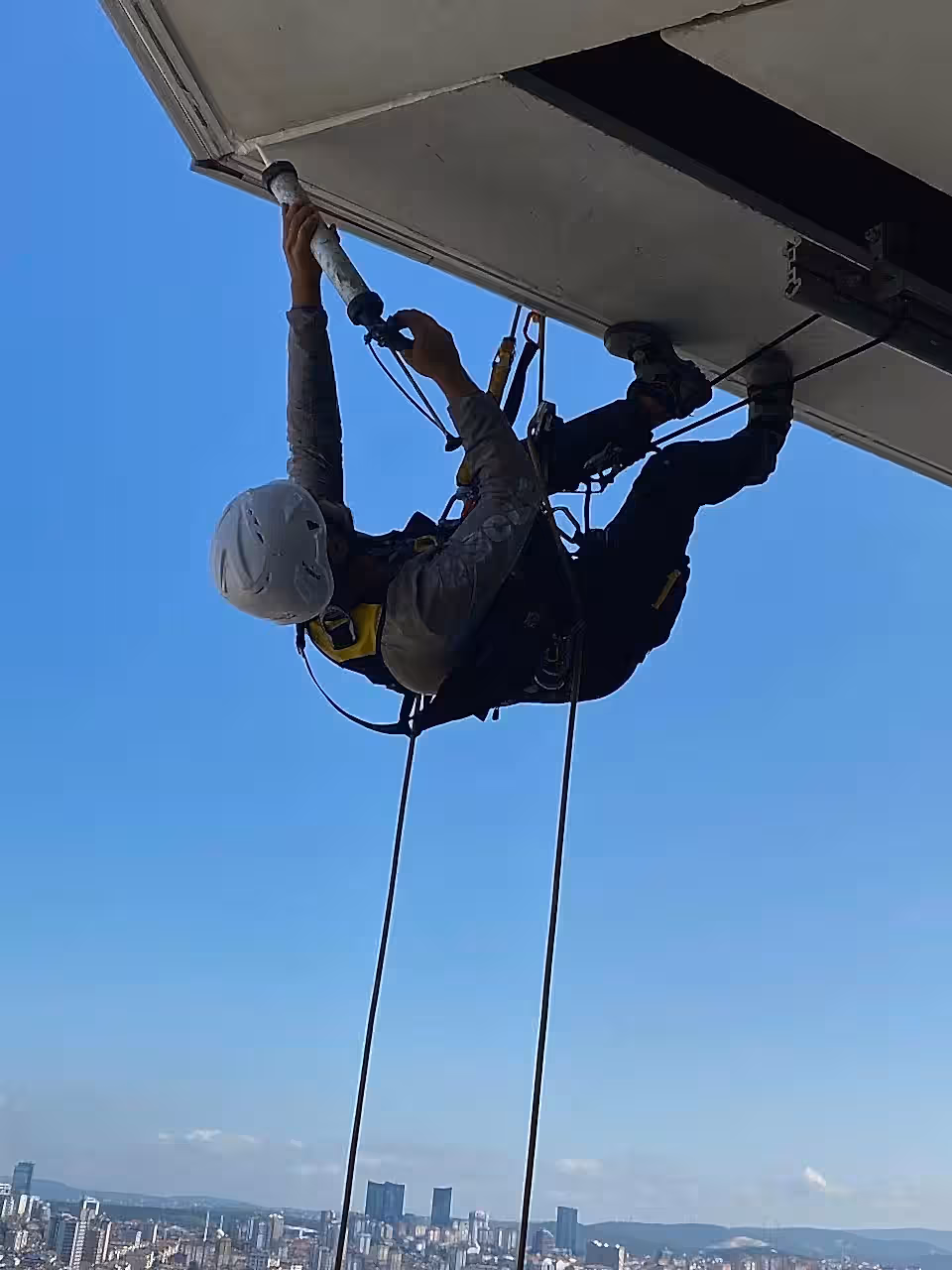 İple erişim uzmanı tarafından yüksek binada gerçekleştirilen dış cephe beton tamiri ve taş duvar onarım çalışması.